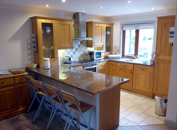 Een moderne keuken met houten kastjes, een centraal eiland met barkrukken, een magnetron en een gasfornuis.