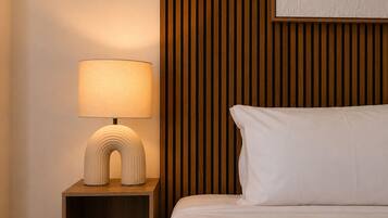 Habitación de hotel ordenada con lámpara de noche, cama con ropa blanca y pared de paneles de madera.