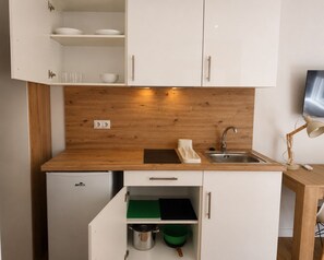 A compact kitchen with white cabinets, a wooden countertop, a built-in sink, and a small refrigerator.