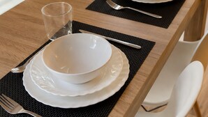 A dining table set with white plates, bowls, cutlery, and glasses, with a black placemat and a white chair. - Aparthotel Fuenlabrada Central (Fuenlabrada)