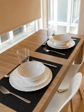 A dining table set with white plates, bowls, cutlery, and glasses, with a black placemat and a white chair.