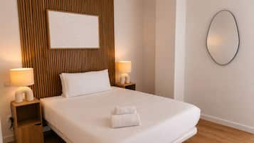 A hotel room with a bed, two bedside lamps, a wall-mounted mirror, and an air conditioning unit.