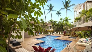 Un espace piscine aménagé avec des chaises longues et une petite piscine, le tout entouré de palmiers et de verdure.