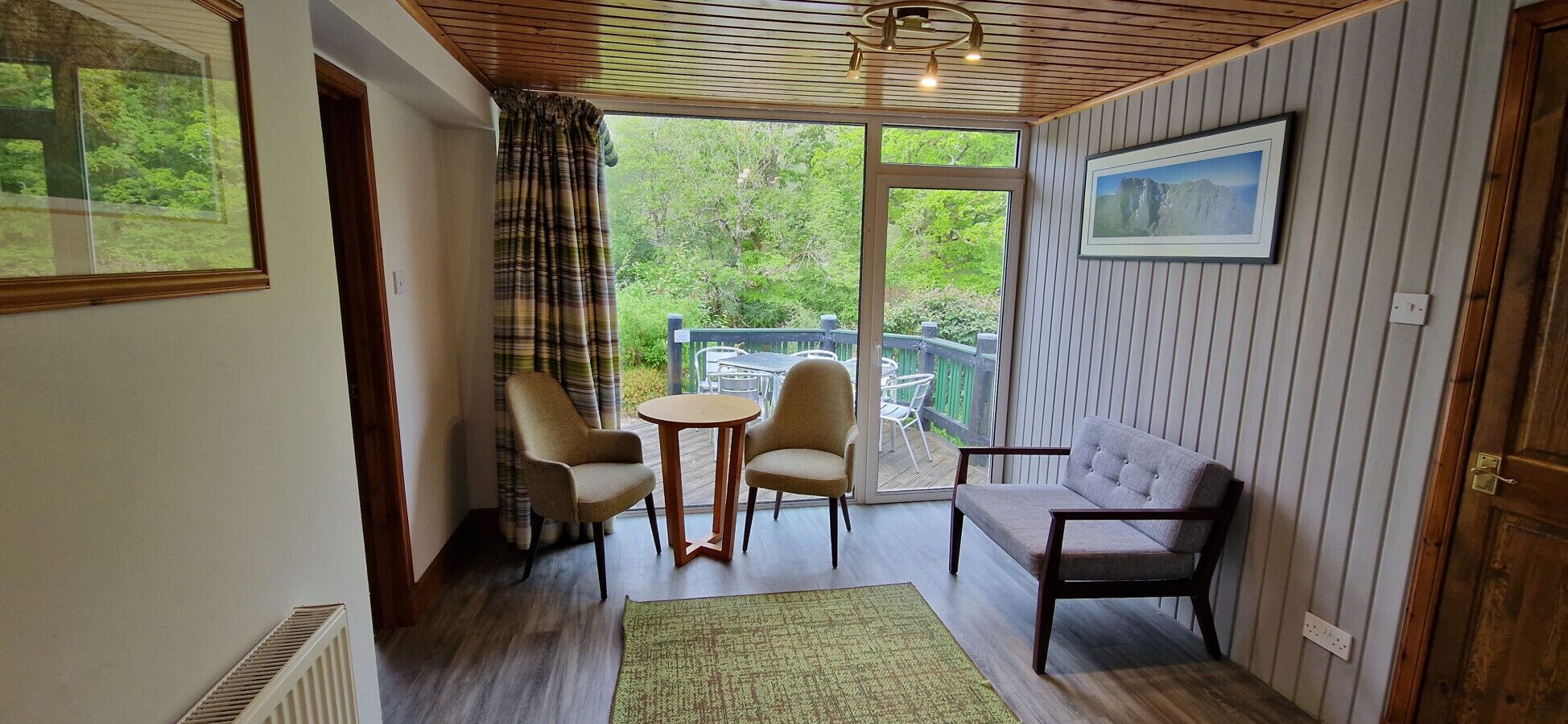 Una habitación con techo de madera, un sofá, dos sillones, una mesita y vistas a zonas verdes a través de una ventana.
