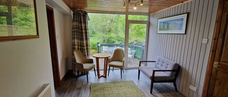 Una habitación con techo de madera, un sofá, dos sillones, una mesita y vistas a zonas verdes a través de una ventana.