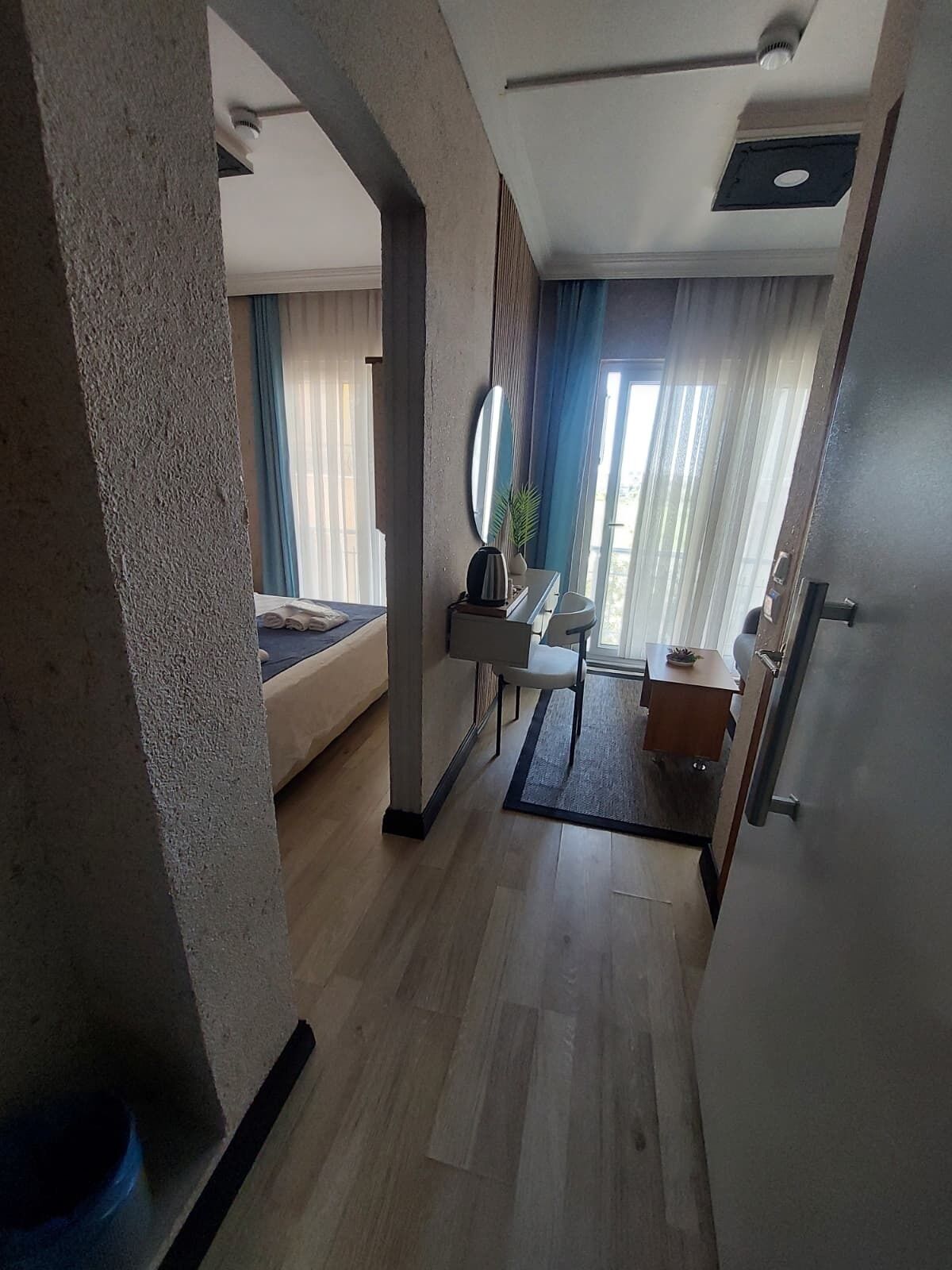 Quarto de hotel moderno com cama, escrivaninha, poltrona e vista para o exterior através de grandes janelas.