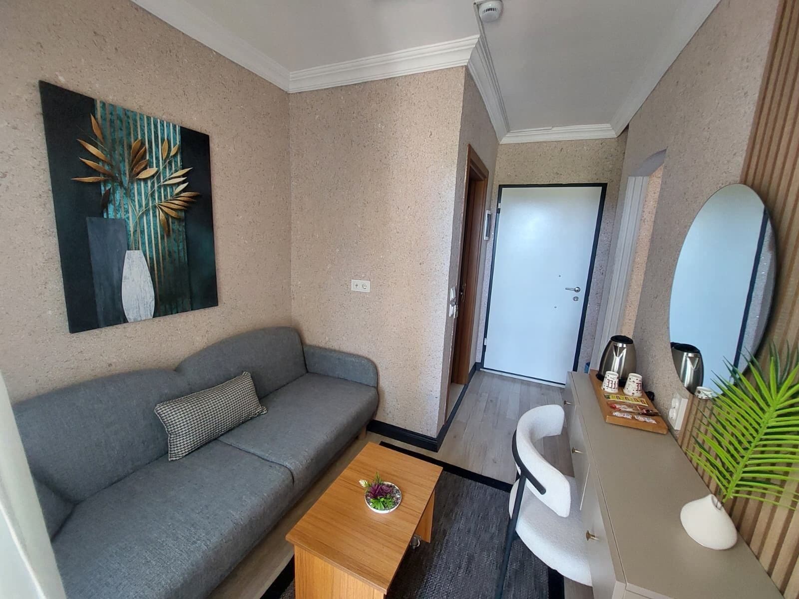 A compact living space with a gray sofa, a wooden coffee table, a white chair, a small side table with a plant, and a painting on the wall.