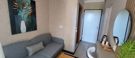 A compact living space with a gray sofa, a wooden coffee table, a white chair, a small side table with a plant, and a painting on the wall.
