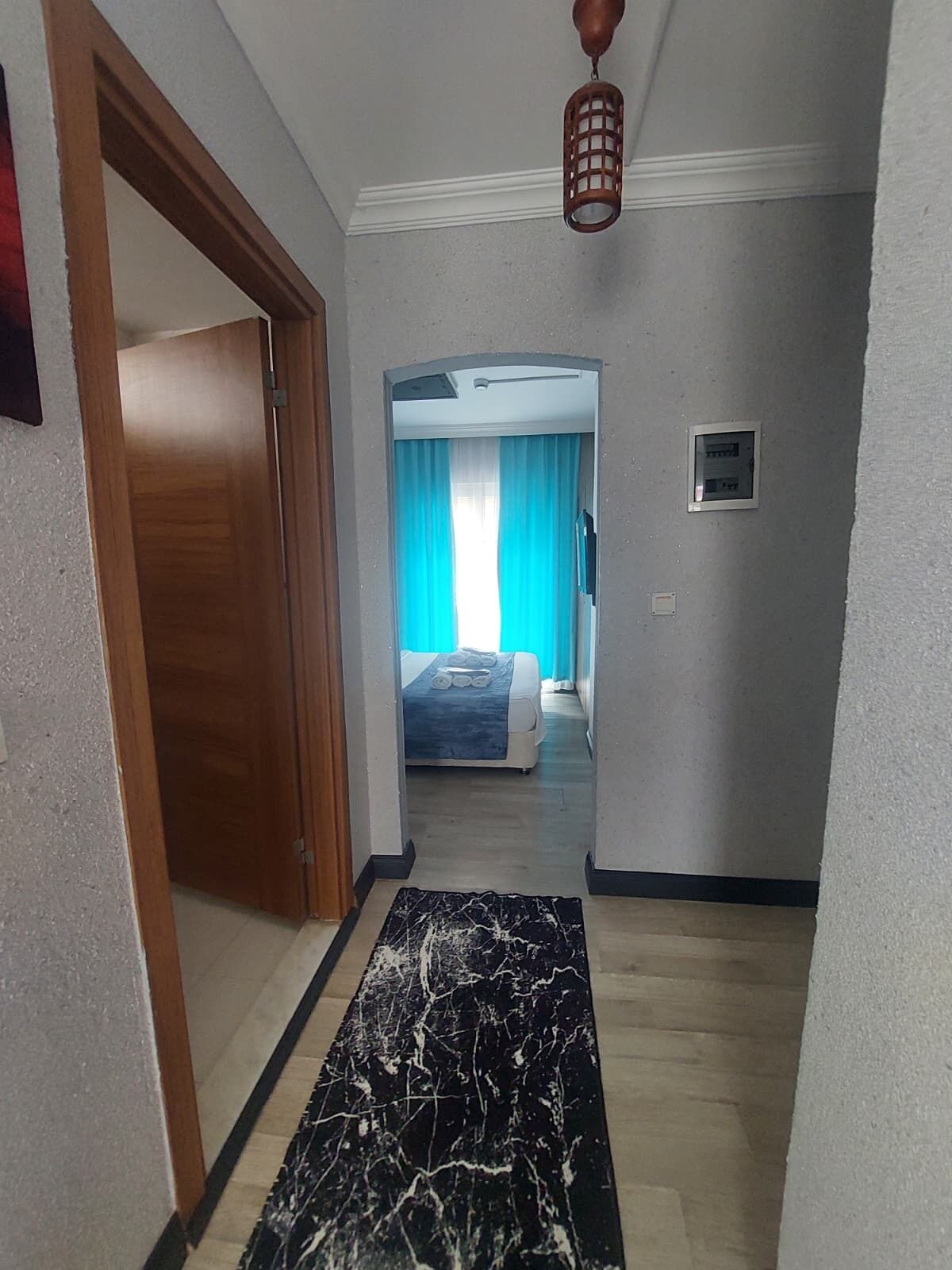 A hallway leading to a bedroom with a bed, a ceiling fan, and a wall-mounted light fixture.