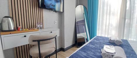 A hotel room with a bed, a desk with a chair, a television, a mirror, and a window with curtains.