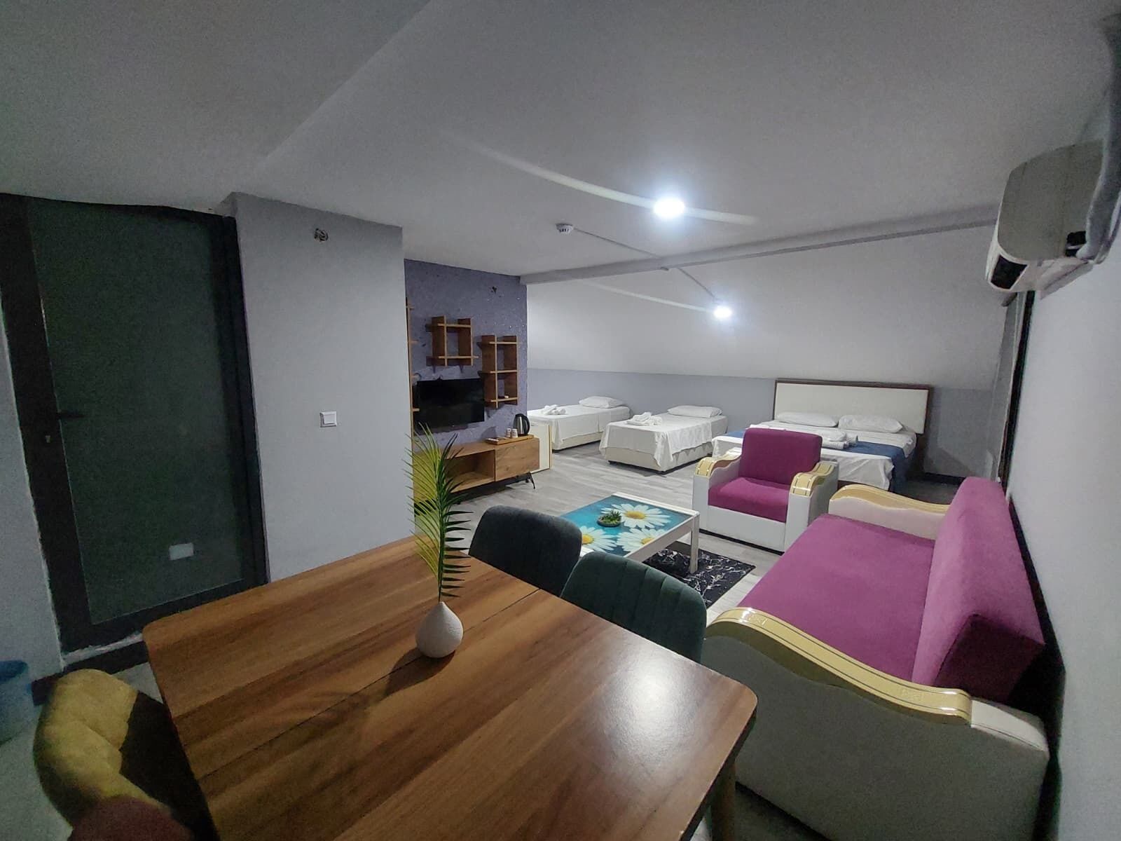 A hotel room with a wooden dining table, a sofa, a bed, and a TV.