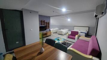 A hotel room with a wooden dining table, a sofa, a bed, and a TV.