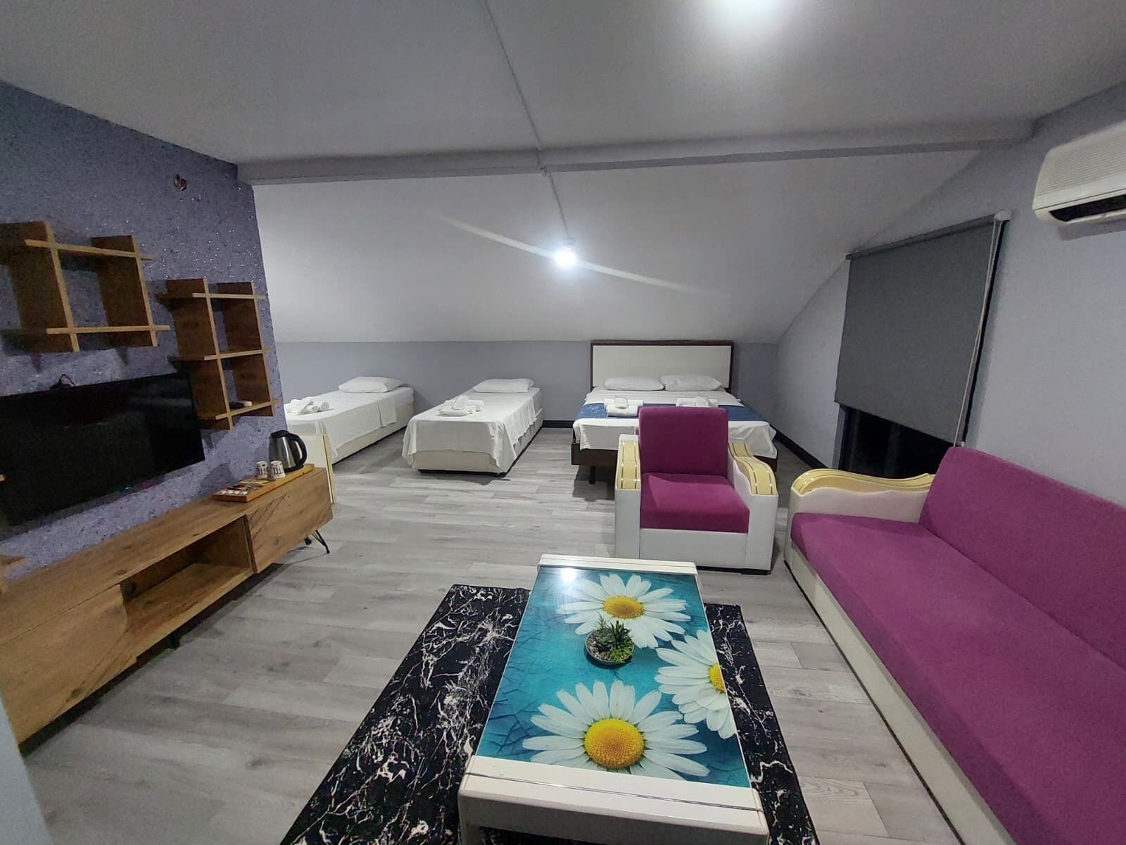 A modern living room with a flat-screen TV, a coffee table with a floral design, a sofa, a bed, and a TV stand.