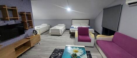 A modern living room with a flat-screen TV, a coffee table with a floral design, a sofa, a bed, and a TV stand.