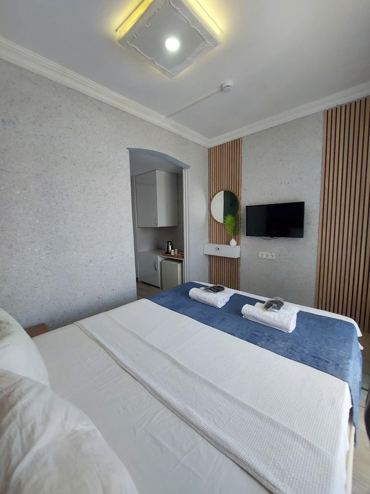 A hotel room with a bed, a TV, a mirror, and a small kitchenette.