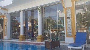 A hotel with a swimming pool, large glass windows, and a blue lounge chair. - dolunaydın otel (Manavgat)