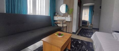 Una habitación de hotel moderna con sofá, una mesita de centro de madera, una cama, un baño con lavamanos y un espejo.