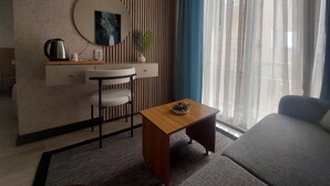 A modern living room with a sofa, a coffee table, a desk with a chair, a round mirror, and a plant. - dolunaydın otel (Manavgat)