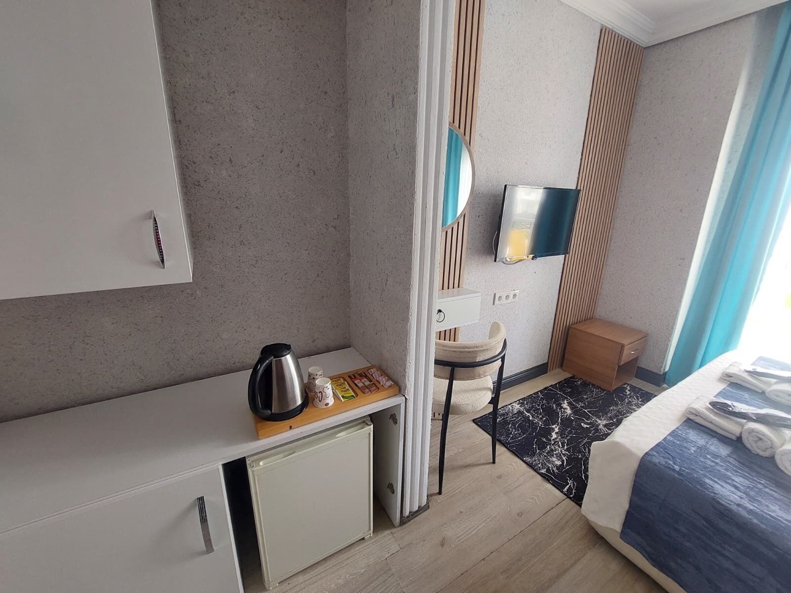 Una habitación de hotel pequeña con kitchenette, una cama, una mesita, una silla, un espejo y un televisor.