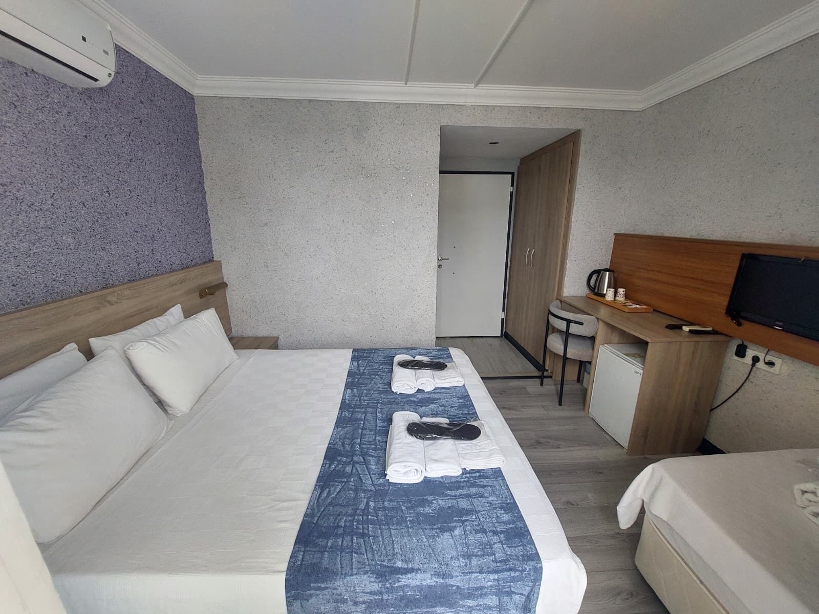 Habitación de hotel con cama, escritorio, silla, televisor y aire acondicionado.