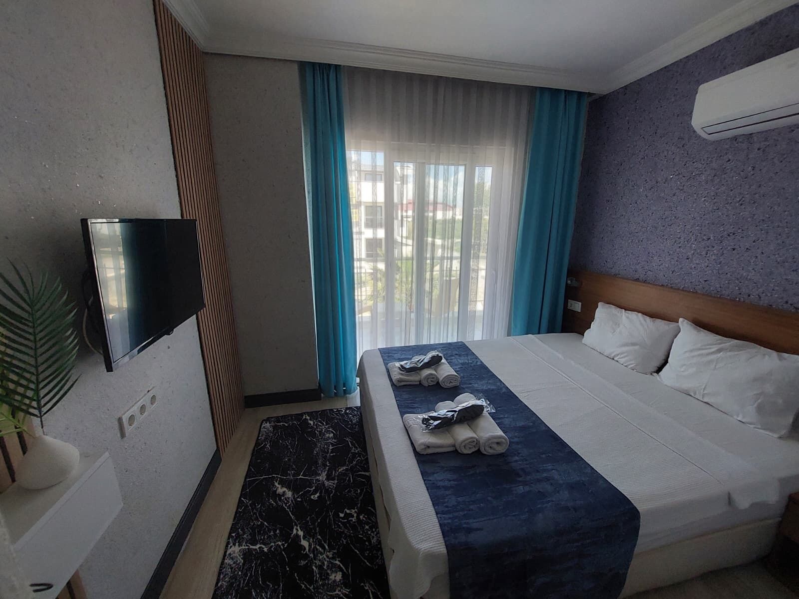 Une chambre d’hôtel avec un lit, un téléviseur à écran plat, une plante en pot et une vue sur l’extérieur.