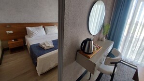 A hotel room with a bed, a desk with a chair, a mirror, and a window with curtains. - dolunaydın otel (Manavgat)