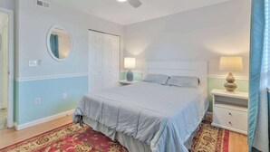 Ein Schlafzimmer mit einem Bett, zwei Nachttischen, einem Deckenventilator, einem Spiegel und einer Tür.