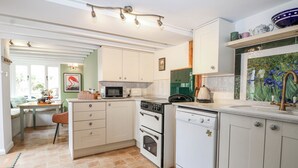 A compact kitchen with white cabinets, a microwave, stove, and dishwasher. - Quince Cottage (Lewes)
