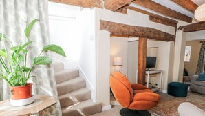 A living room with a staircase, a potted plant, a sofa, and a television. - Quince Cottage (Lewes)
