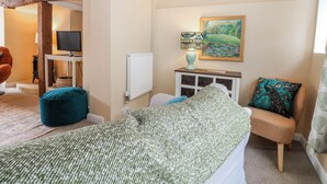 A bedroom with a bed, a chair, a lamp, a painting, and a radiator. - Quince Cottage (Lewes)