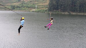 Two individuals engaged in a water activity, connected by a rope over a body of water, with a hilly landscape in the background.