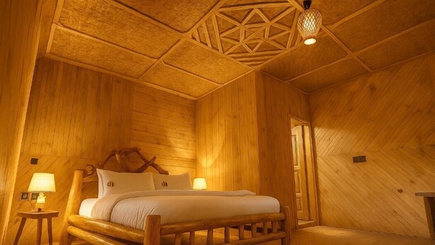 A wooden room with a bed, two bedside lamps, and a geometric ceiling design.