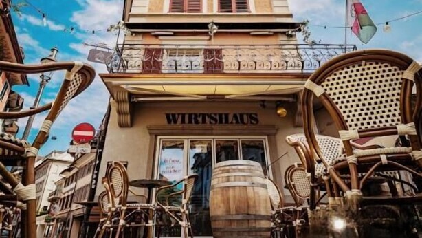 A building with a sign 'WIRTSHAUS' and wicker furniture outside. - KBCityRooms (Lucerne)