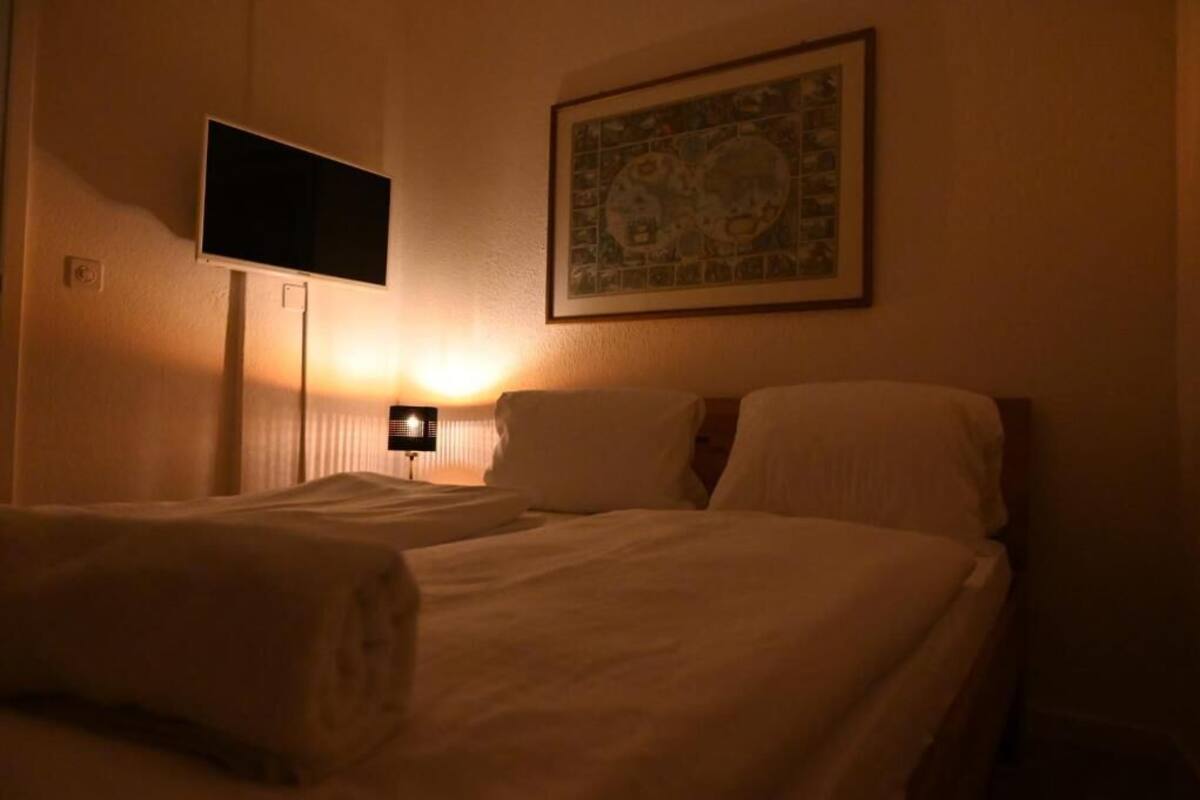 A hotel room with two beds, a television mounted on the wall, a framed picture above the beds, and a bedside lamp.
