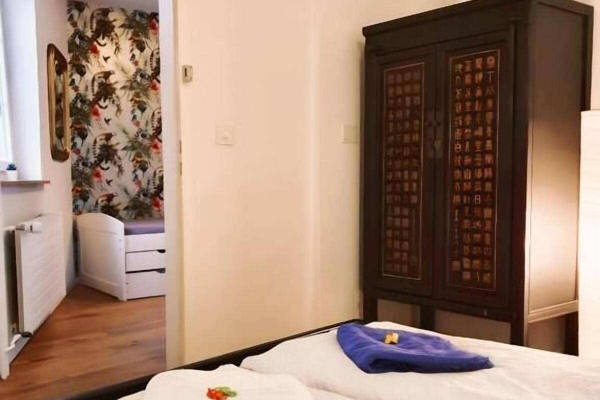 A hotel room with two beds, a wardrobe, a bathroom with a shower, and a floral wallpapered wall.