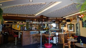 A bar area with a wooden counter, stools, and a variety of bottles and glasses. - KBCityRooms (Lucerne)
