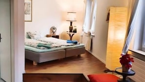 A compact hotel room with a bed, bedside table, lamp, and a window with curtains. - KBCityRooms (Lucerne)