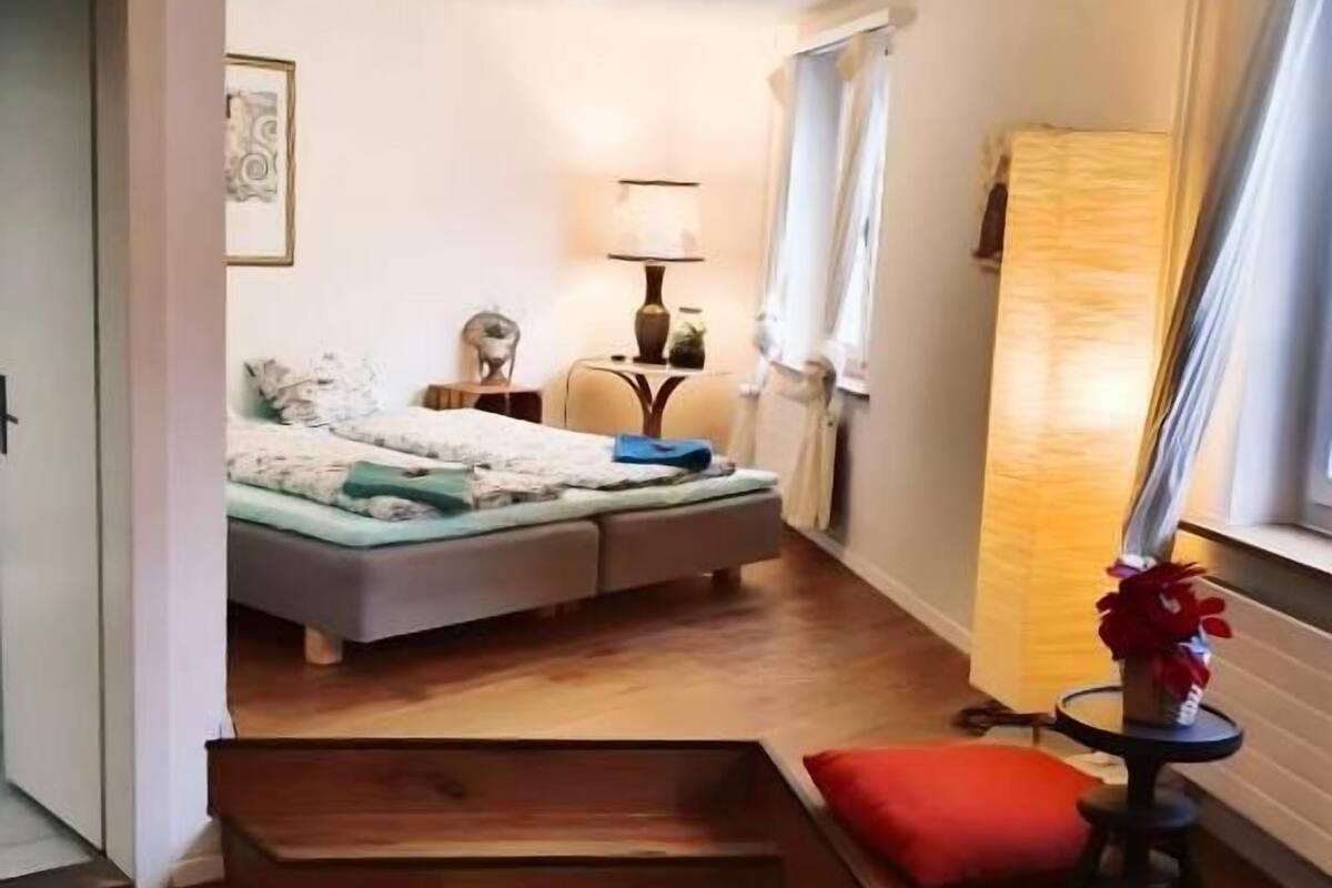 A compact hotel room with a bed, bedside table, lamp, and a window with curtains.