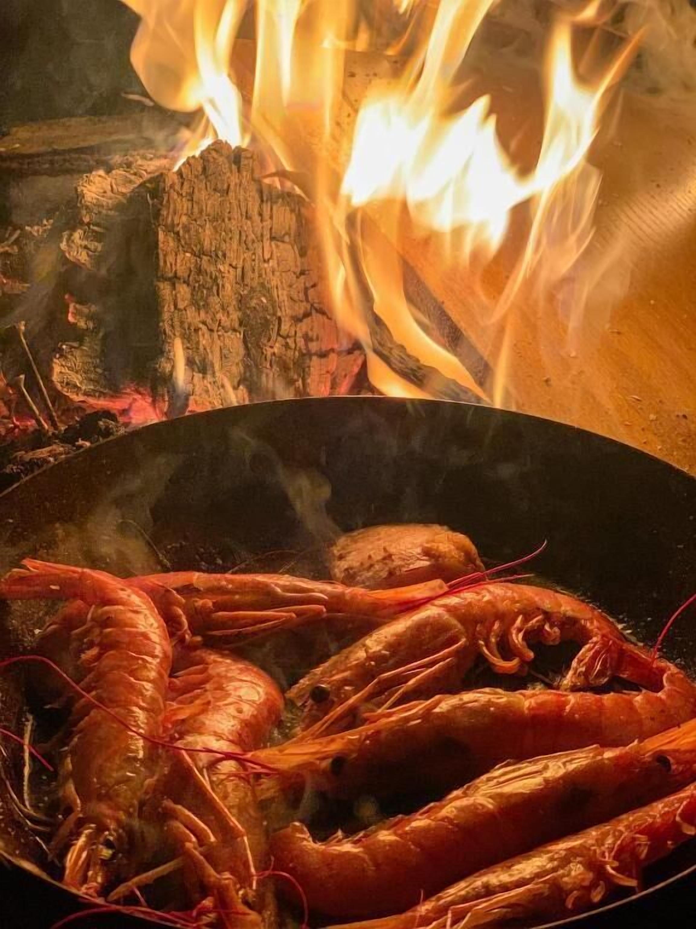Una sartén con camarones cocidos y un fuego al fondo.
