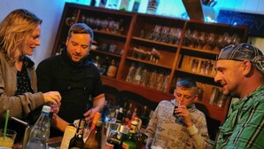 A bar area with bottles and glasses, a person pouring a drink, and shelves with various items.
