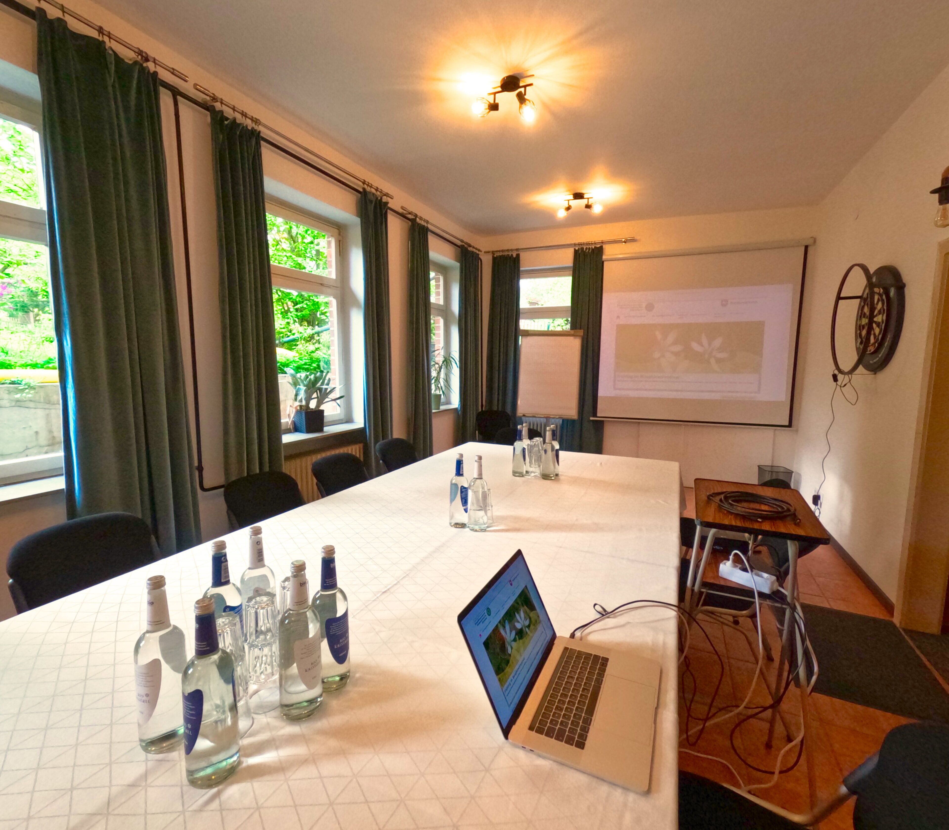 Sala de conferências com uma mesa comprida, laptops e garrafas de água.