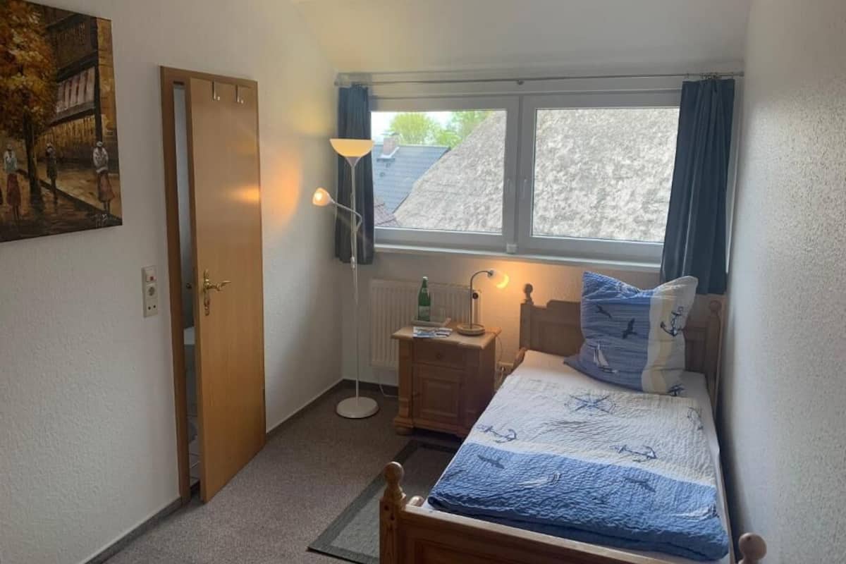 A bedroom with a bed, a nightstand, a lamp, a window, and a door.