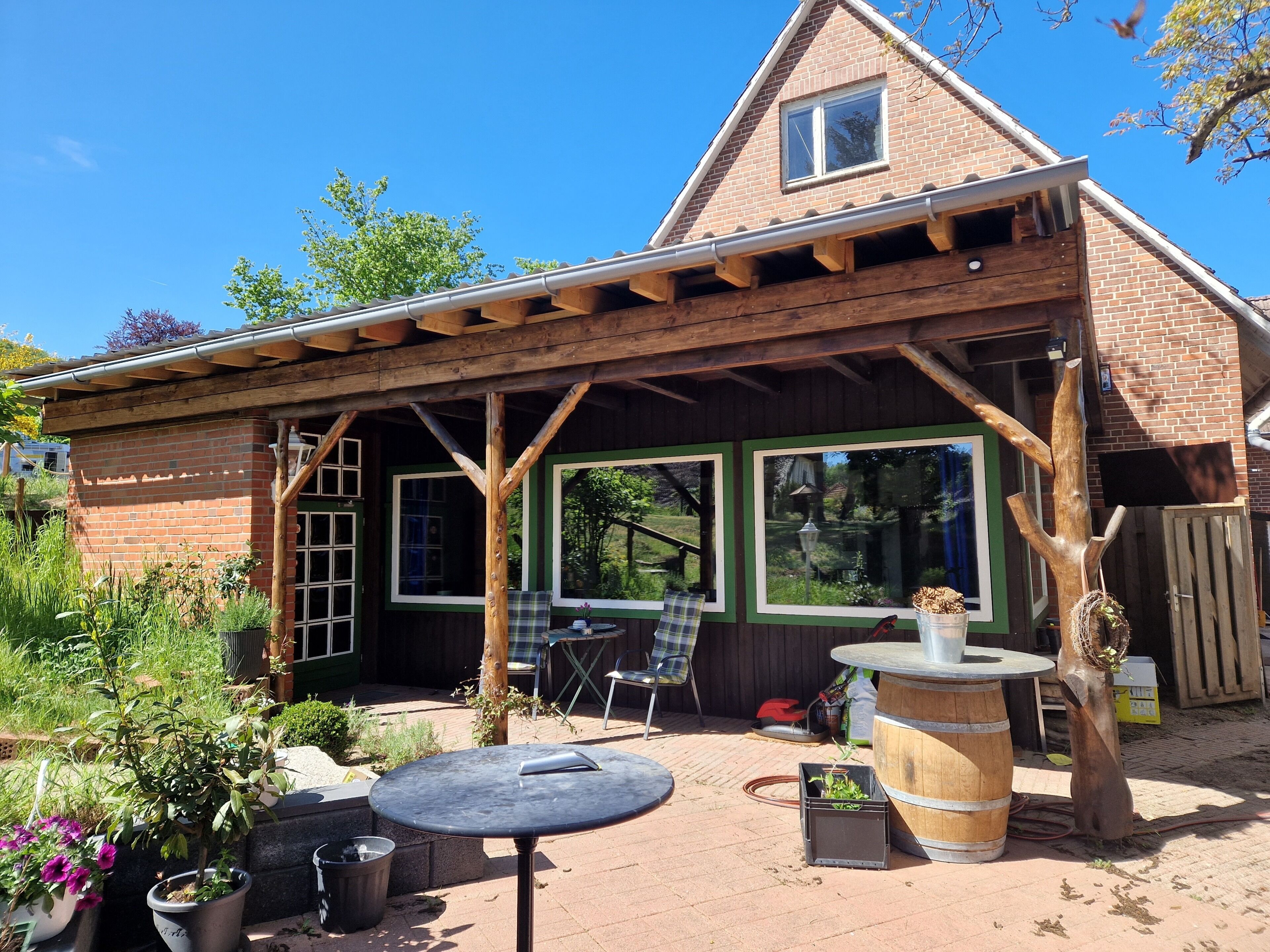 Una casa de ladrillo con un porche de madera, una mesa, sillas y plantas en macetas.