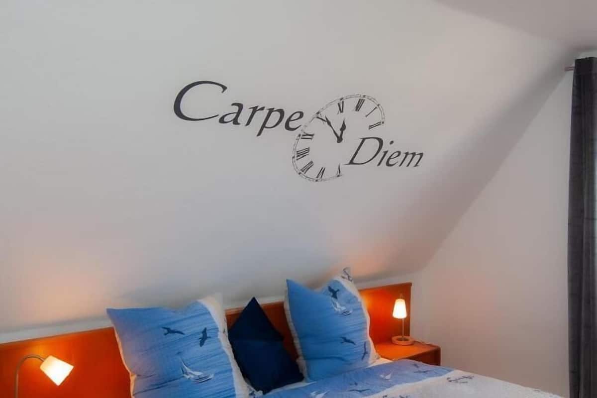 A bedroom with a bed, two bedside tables, a wall clock, and a wall-mounted sign.