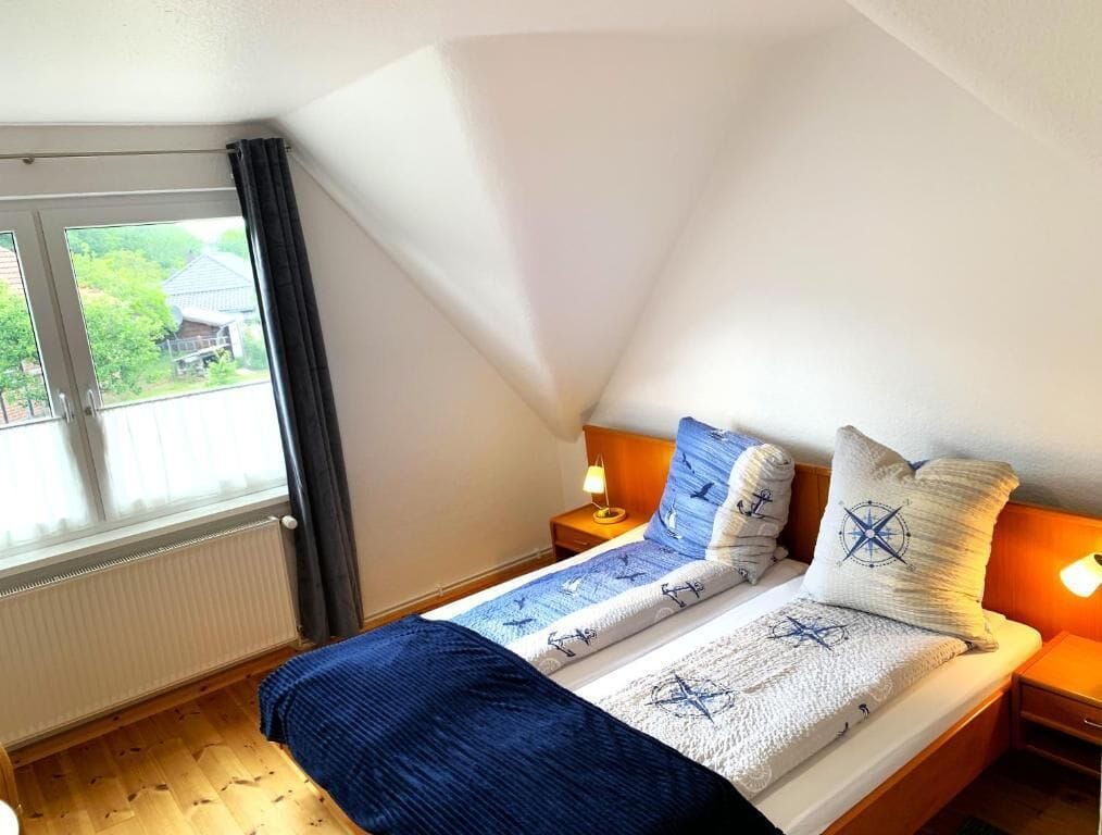 A bedroom with a bed, two bedside tables, a window, and a radiator.