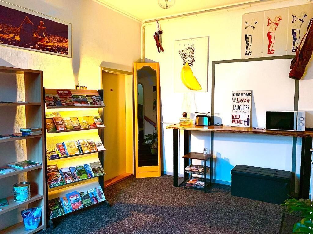 Una habitación con una estantería, un escritorio con una computadora, un microondas y una cita enmarcada en la pared.
