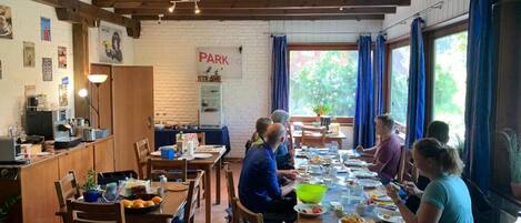 A communal dining area with wooden tables and chairs, a kitchen area with appliances, and a sign indicating a parking area.