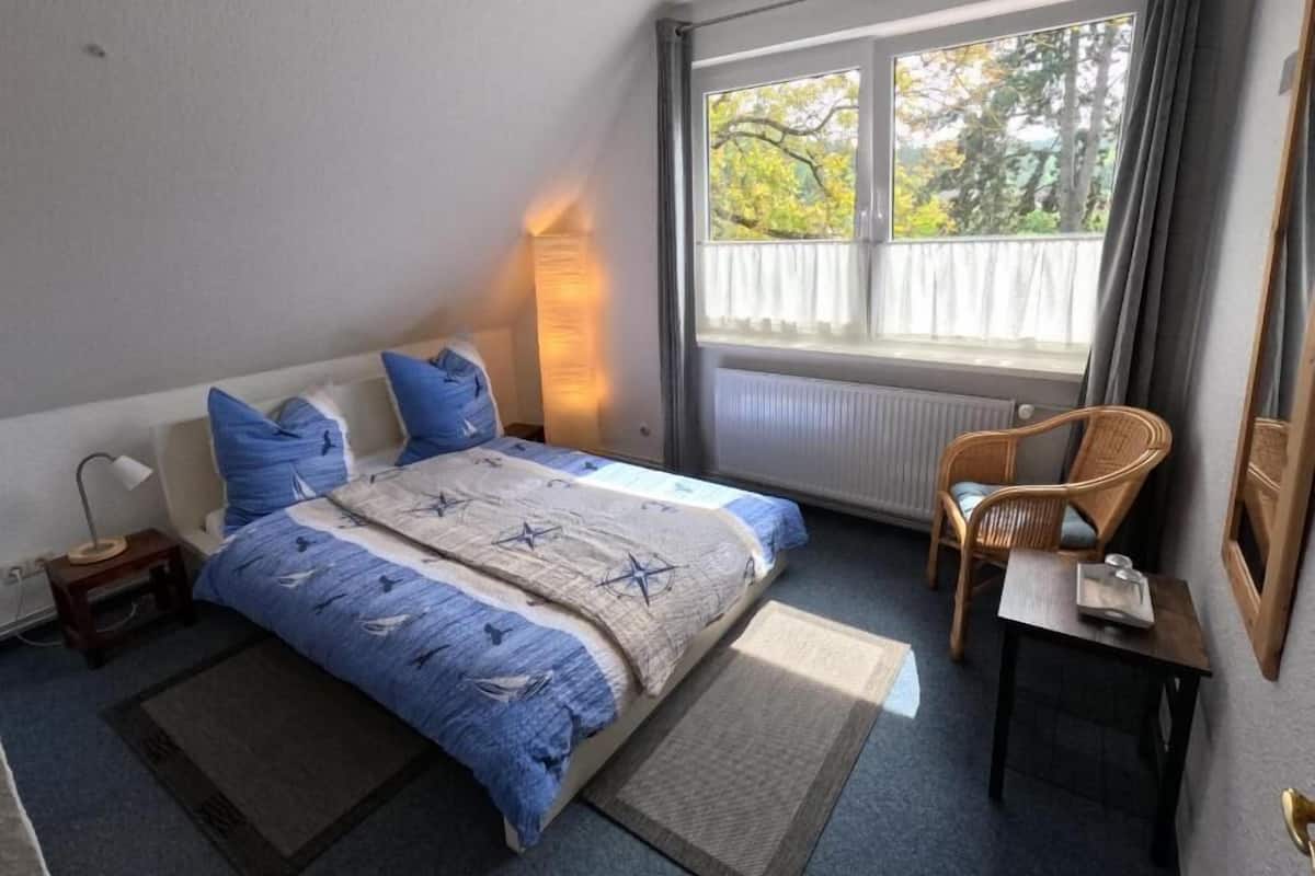 A bedroom with a bed, a chair, a desk, a lamp, and a window with curtains.