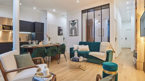 Una sala de estar moderna con comedor, un sofá color aguamarina y una cocina con armarios oscuros.