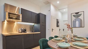 Una cocina moderna con armarios oscuros, una campana extractora de acero inoxidable y un comedor con una mesa redonda dispuesta para cuatro comensales.